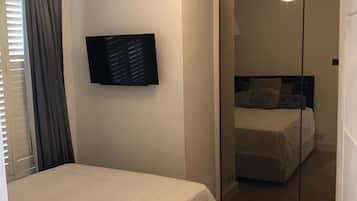 A bedroom with a bed, a TV mounted on the wall, a mirror, and a ceiling light.