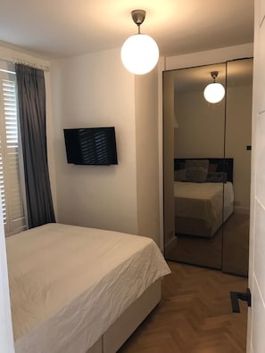 Ein Schlafzimmer mit einem Bett, einem an der Wand montierten Fernseher, einem Spiegel und einer Deckenleuchte.