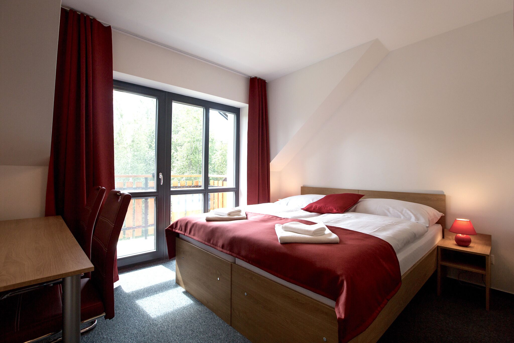 Un dormitorio con cama, escritorio y ventana con cortinas.