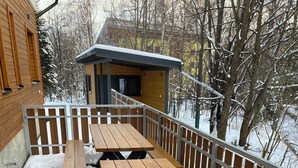 A wooden deck with picnic tables, a metal railing, and a building in the background. - Vila DEDO (Vysoké Tatry)