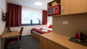 A hotel room with a bed, a desk with a chair, a microwave, a kettle, and a window with curtains. - Vila DEDO (Vysoké Tatry)
