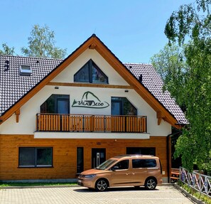 A two-story building with a wooden facade, a balcony, and a car parked in front. - Vila DEDO (Vysoké Tatry)