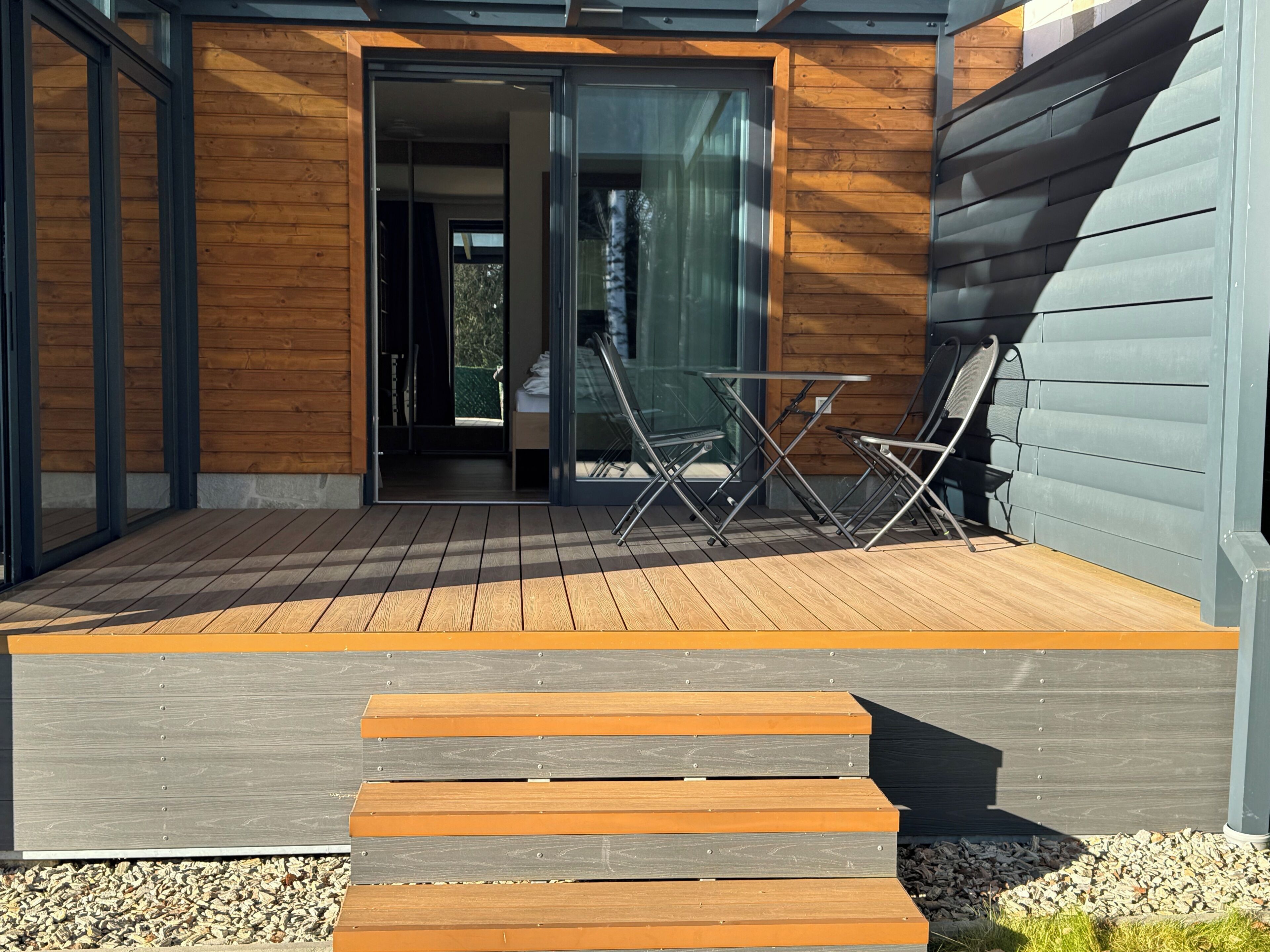 A modern house with a wooden deck, a glass door entrance, and outdoor furniture.