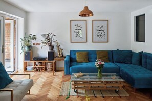Ein modernes Wohnzimmer mit einem blauen Sofa, einem Glastisch und Holzboden.