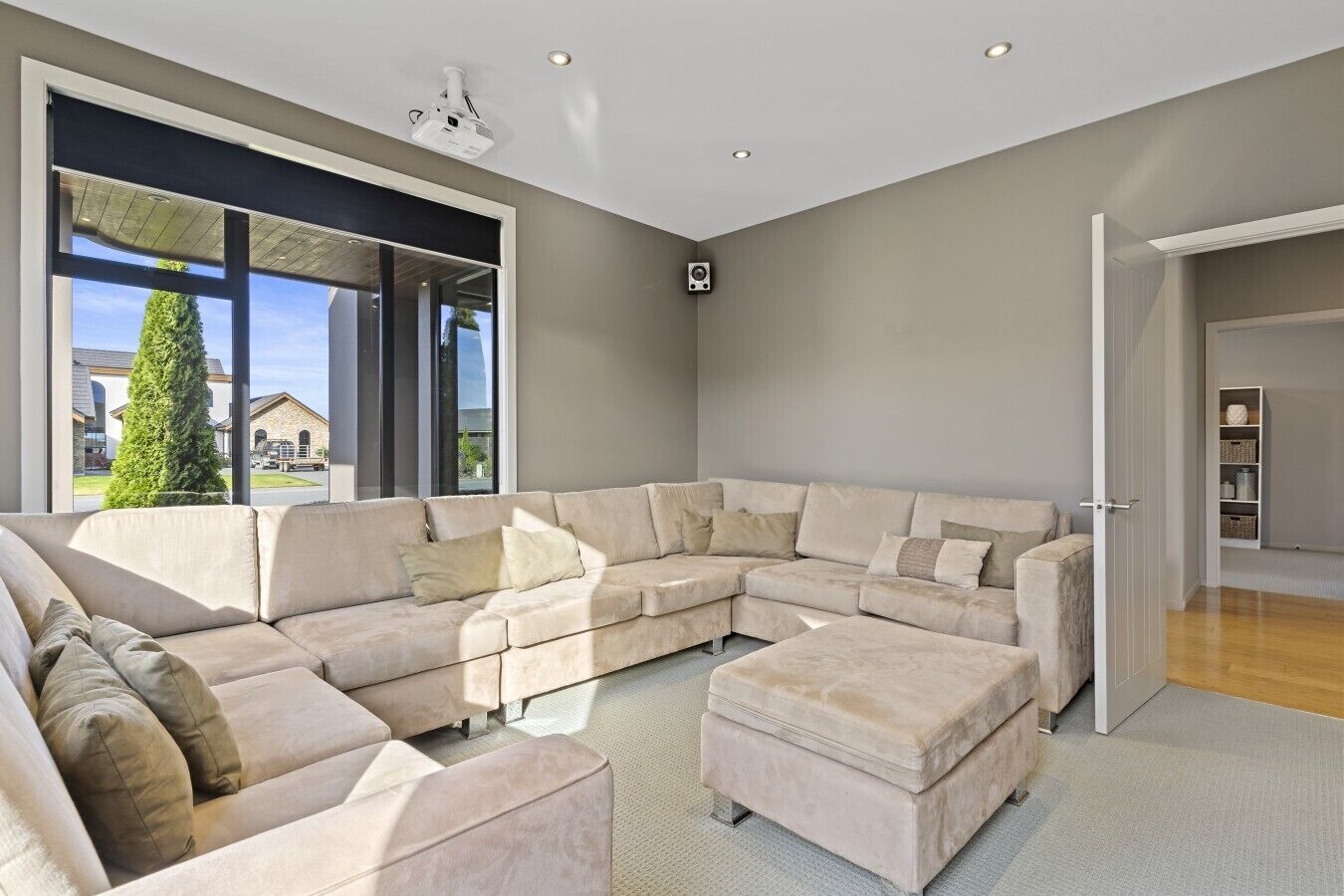 A modern living room with a sectional sofa, a large window, and a door leading to another room.
