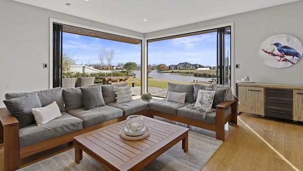 Una sala de estar moderna con un sofá modular, una mesa de centro de madera y vista a un lago y casas.