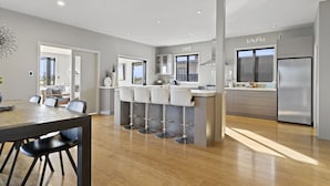Una cocina moderna con una isla central, taburetes de bar, electrodomésticos de acero inoxidable y un comedor con mesa y sillas.