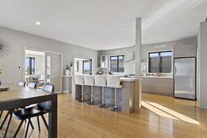 Een moderne keuken met een centraal eiland, barstoelen, roestvrijstalen apparatuur en een eethoek met een tafel en stoelen.