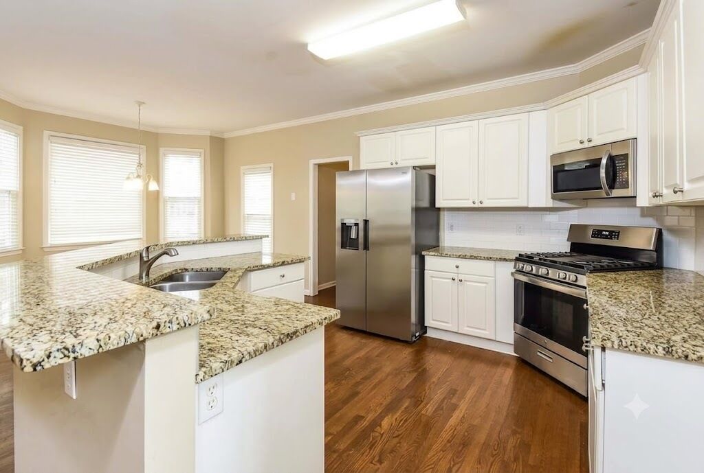 A kitchen with white cabinets, granite countertops, stainless steel appliances, and wooden flooring.