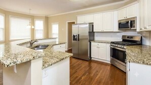 A kitchen with white cabinets, granite countertops, stainless steel appliances, and wooden flooring. - Spacious Brick Home in Acworth – Perfect Family Getaway (Acworth)