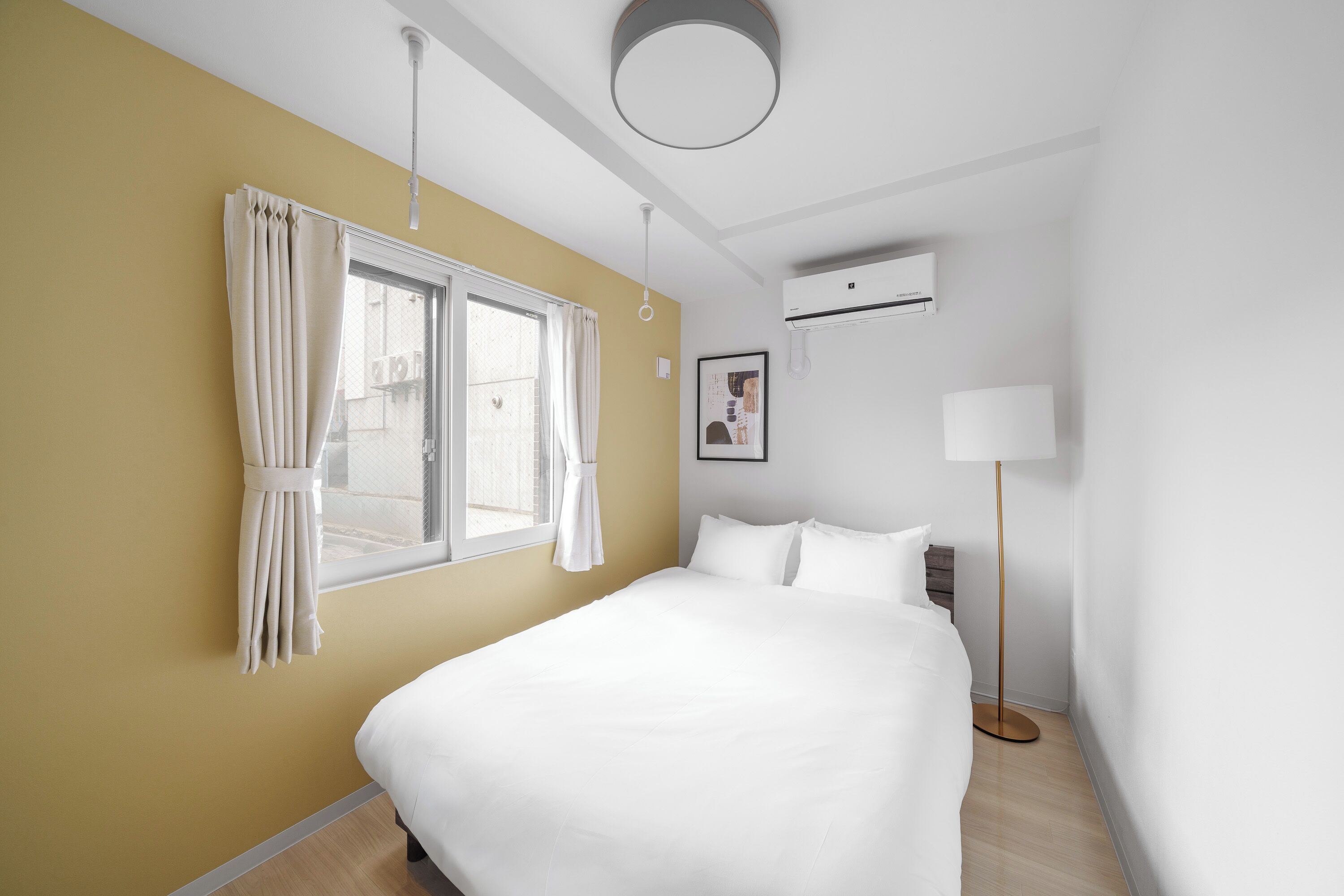 A hotel room with a bed, a window with curtains, a bedside table, a lamp, and an air conditioning unit.