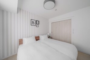 A bedroom with a bed, a nightstand, a wall-mounted light, and a door. - PREGARE 103 (Sapporoshi)