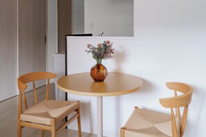 A round wooden table with a vase of flowers, two wooden chairs with woven seats, and a white wall with a door and a mirror. - PREGARE 103 (Sapporoshi)
