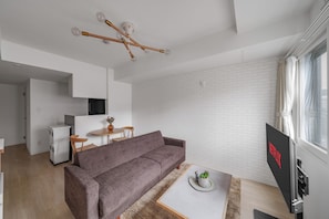 A modern living room with a grey sofa, a coffee table with a plant, a TV mounted on a wall, and a white brick wall. - PREGARE 103 (Sapporoshi)