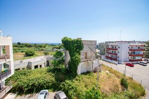 Un immeuble à plusieurs étages doté d’un parking, bordé par une route et offrant une vue sur la mer.