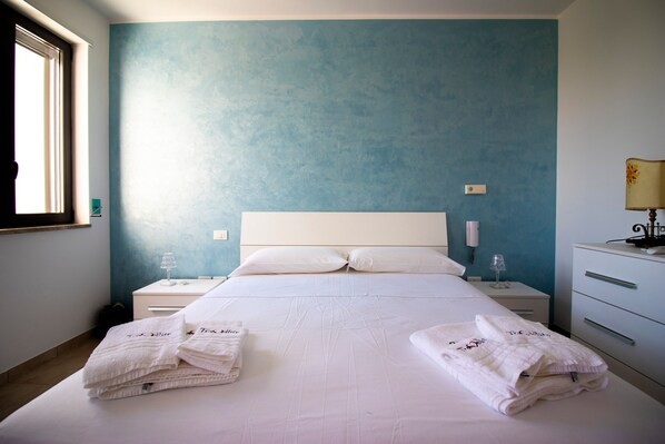 Une chambre d’hôtel avec un grand lit, deux tables de chevet, une fenêtre et une petite table de nuit avec une lampe.