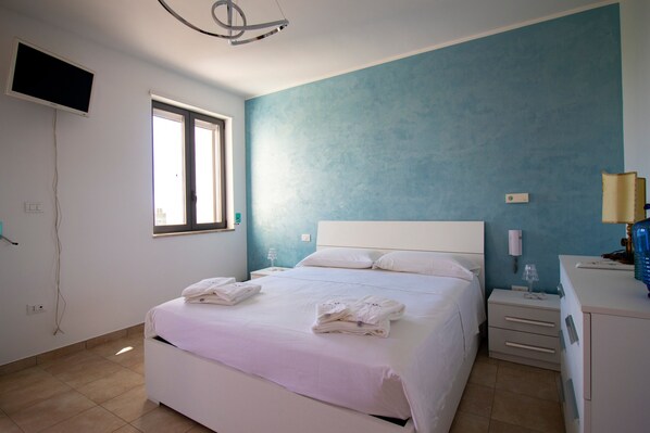 A bedroom with a bed, bedside tables, a TV, and a window.
