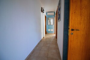 Un couloir avec une porte en bois, un luminaire et un sol carrelé.