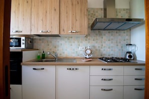 Een keuken met houten kastjes, een gootsteen, een fornuis, een magnetron en een blender.
