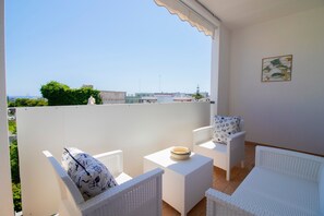 Een balkon met witte rieten meubels, een kleine tafel en een decoratief wandobject.
