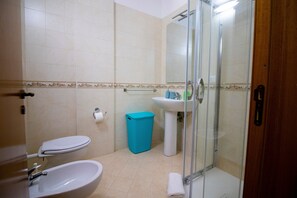 A bathroom with a toilet, sink, shower, and a blue trash bin.