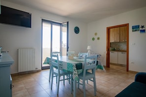 Un'area pranzo con tavolo e sedie, una cucina con mobili in legno, un termosifone e un orologio a parete.