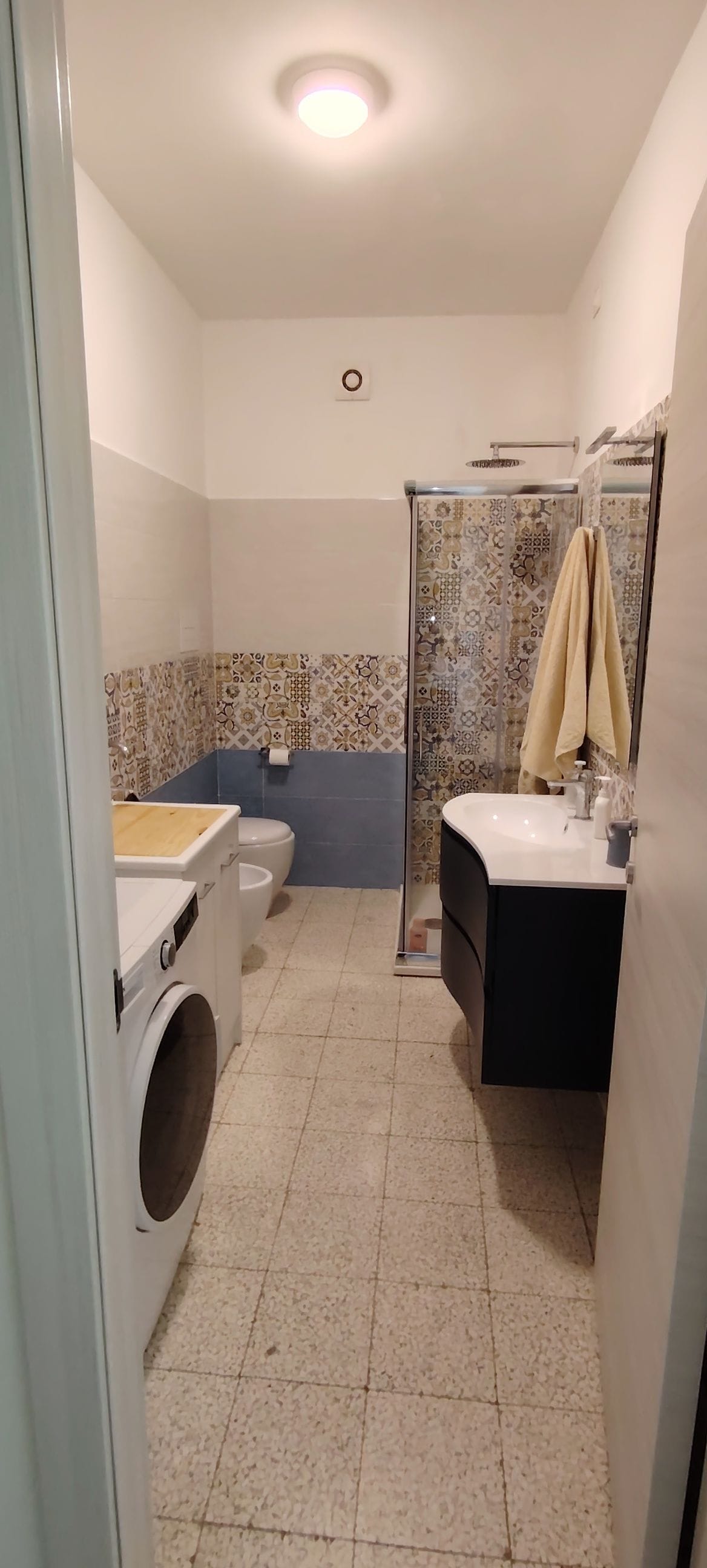 Une petite salle de bain équipée d’un lave-linge, de toilettes, d’un lavabo et d’une douche.