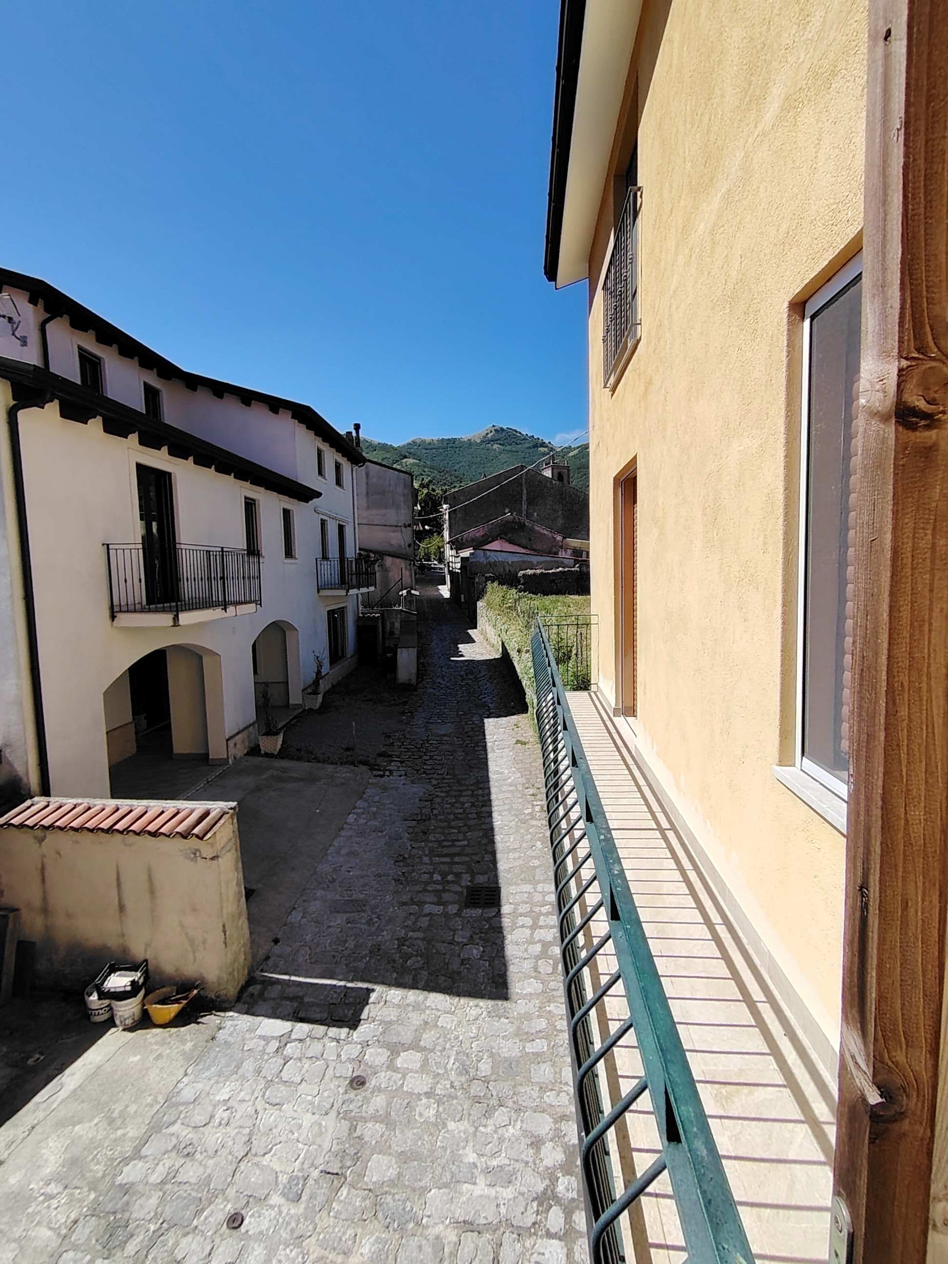 Un stretto vicolo acciottolato tra edifici, con una ringhiera su un lato.