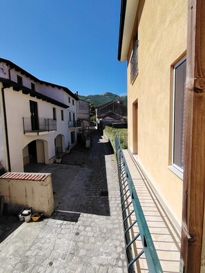 A narrow cobblestone alleyway between buildings with a metal railing on one side.