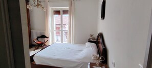 A bedroom with a bed, a chair, a nightstand, and a window with blinds. - CASA DI BIAGIO E MARIA (Trecchina)