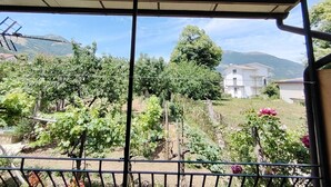 Un balcón con vistas a un viñedo, un edificio blanco y montañas al fondo.