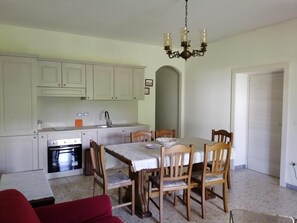A dining area with a table, chairs, a chandelier, and a kitchen with cabinets and appliances. - CASA DI BIAGIO E MARIA (Trecchina)