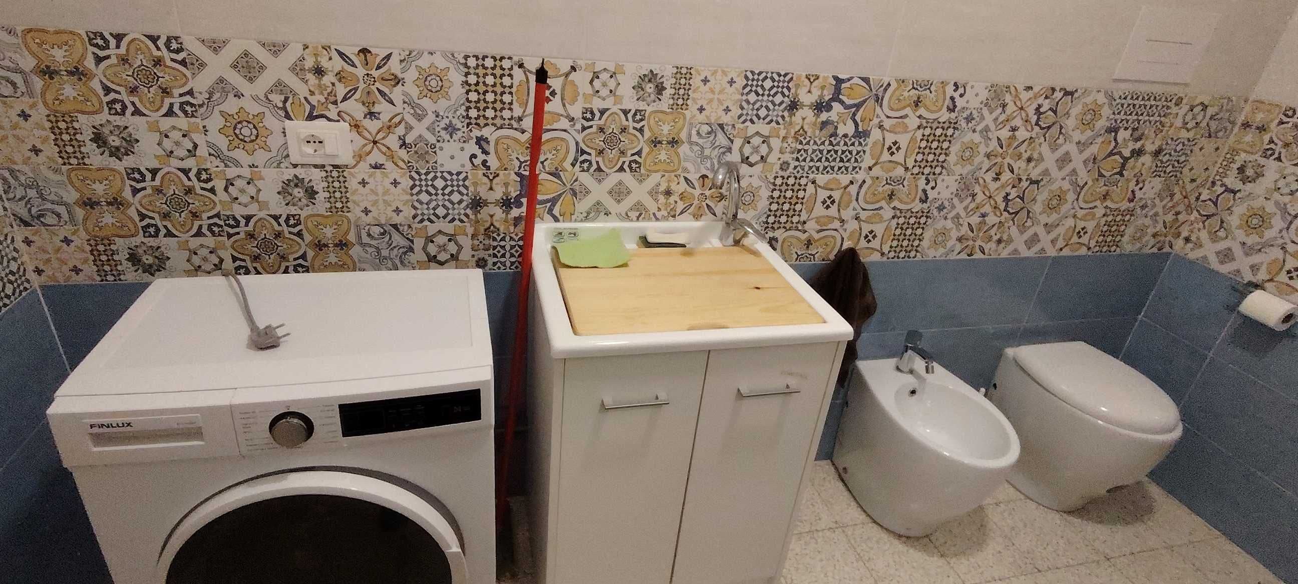 Et badeværelse med vaskemaskine, skab, håndvask og toilet.