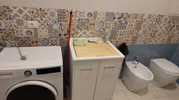 Et badeværelse med vaskemaskine, skab, håndvask og toilet.
