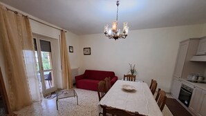 Un comedor con mesa y sillas, un sofá rojo, una lámpara de araña y una cocina al fondo.