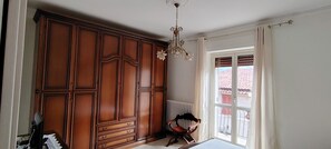 A room with a large wooden wardrobe, a radiator, a chair, and a window with curtains.