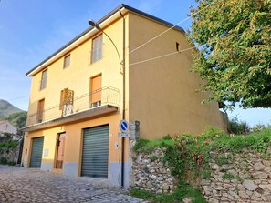 Un edificio de dos pisos con un balcón, una pared de piedra y una calle empedrada.