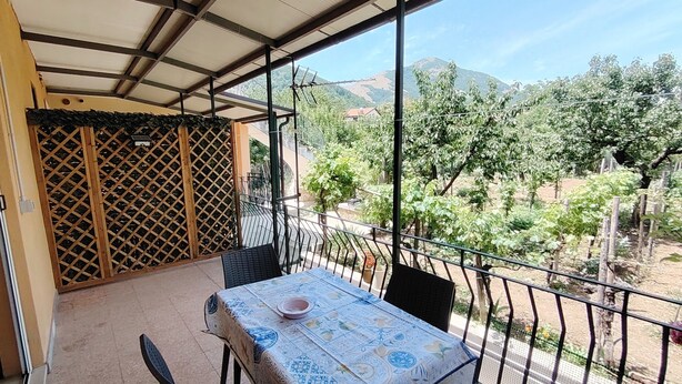 Un balcón techado con mesa y sillas, vistas a un viñedo y un panel de celosía.