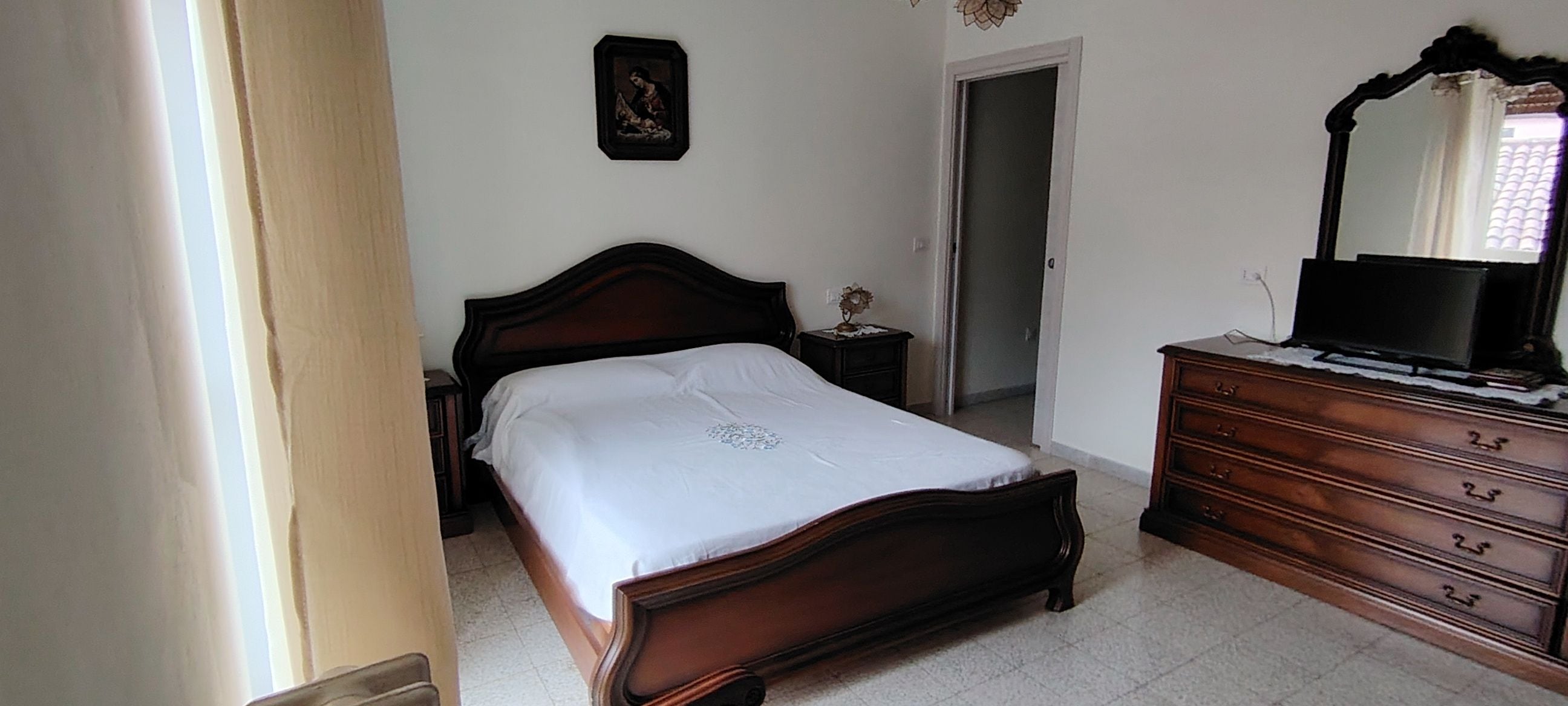 Una camera da letto con un letto di legno, una cassettiera, uno specchio e una porta.