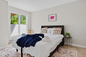 Une chambre à coucher avec un lit, une fenêtre, un tableau encadré et une petite table sur laquelle est posée une plante.