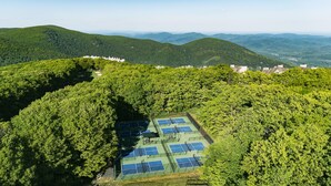 Vue aérienne d’un court de tennis entouré d’une forêt dense et de collines.