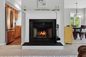 A modern kitchen with a built-in stainless steel refrigerator, wooden cabinets, and a white fireplace with a fire. - Wintergreen Retreat | Golf | Sleeps 12 | Pets OK (Wintergreen Resort)