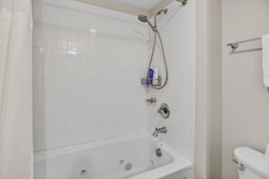 Une salle de bain avec une baignoire blanche, une pomme de douche, des toilettes et un porte-serviettes.
