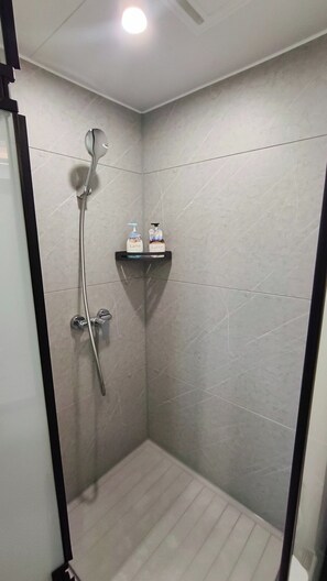 Ducha con cabezal de ducha de mano, grifo empotrado en la pared y repisa con dos botellas etiquetadas 'Latte'.