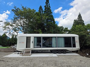 Una caravana blanca con puerta corredera, zona cubierta y una dirección web en el lateral.