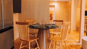 Uma sala de jantar com uma mesa redonda, cadeiras de madeira e uma cozinha moderna ao fundo.