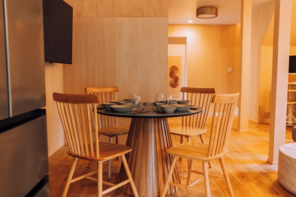 A dining area with a round table, wooden chairs, and a modern kitchen in the background.