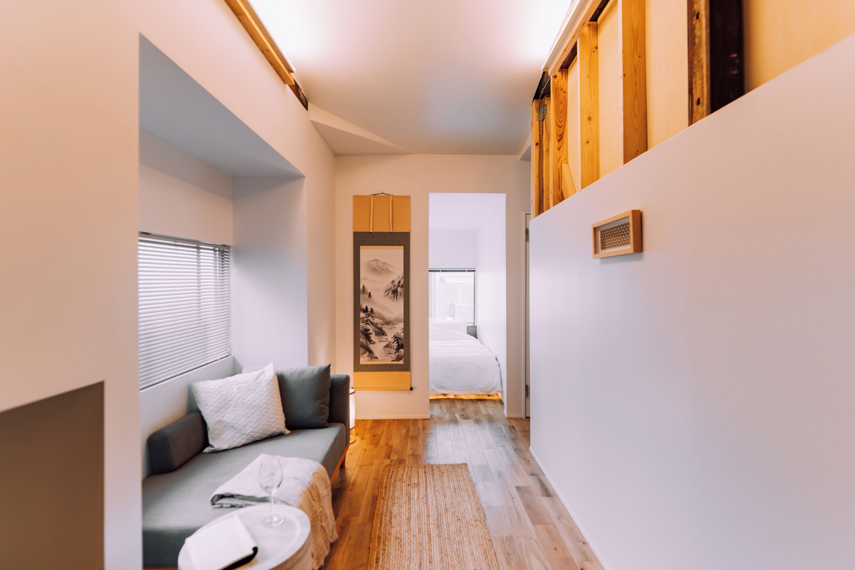 A narrow hallway with a sofa, a small round table, and a bed in the background.