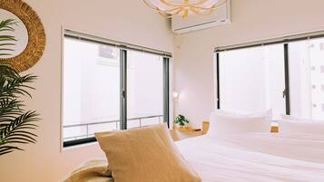 A hotel room with a bed, a large window, a wall-mounted air conditioner, and a hanging light fixture.