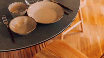 A round table with plates, bowls, and cutlery. There are wooden chairs around the table.